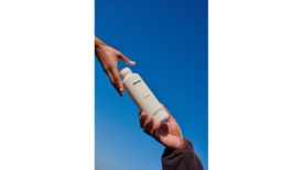 Image of Cove's water bottle with two hands holding it on opposite ends over a blue sky background