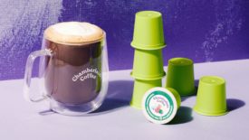 Chamberlain Coffee coffee pods next to a transparent mug of coffee on a purple background