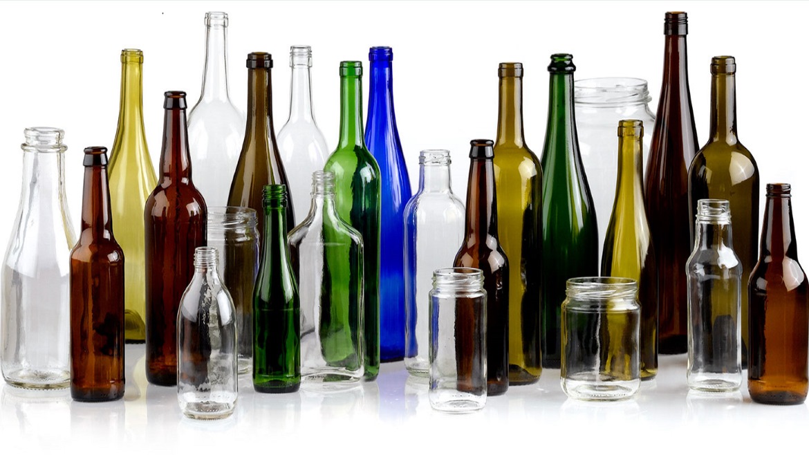 Image of glass bottles in multple colors, shapes and sizes lined up in front of a white background