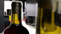 A wine bottle passing through a laser spectroscopy machine for post-bottling quality control