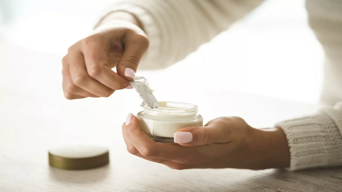 A person is opening the liner of a beauty product in a glass jar.