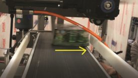 The carrier tray being swept by the conveyor's servo-driven overhead transfer.