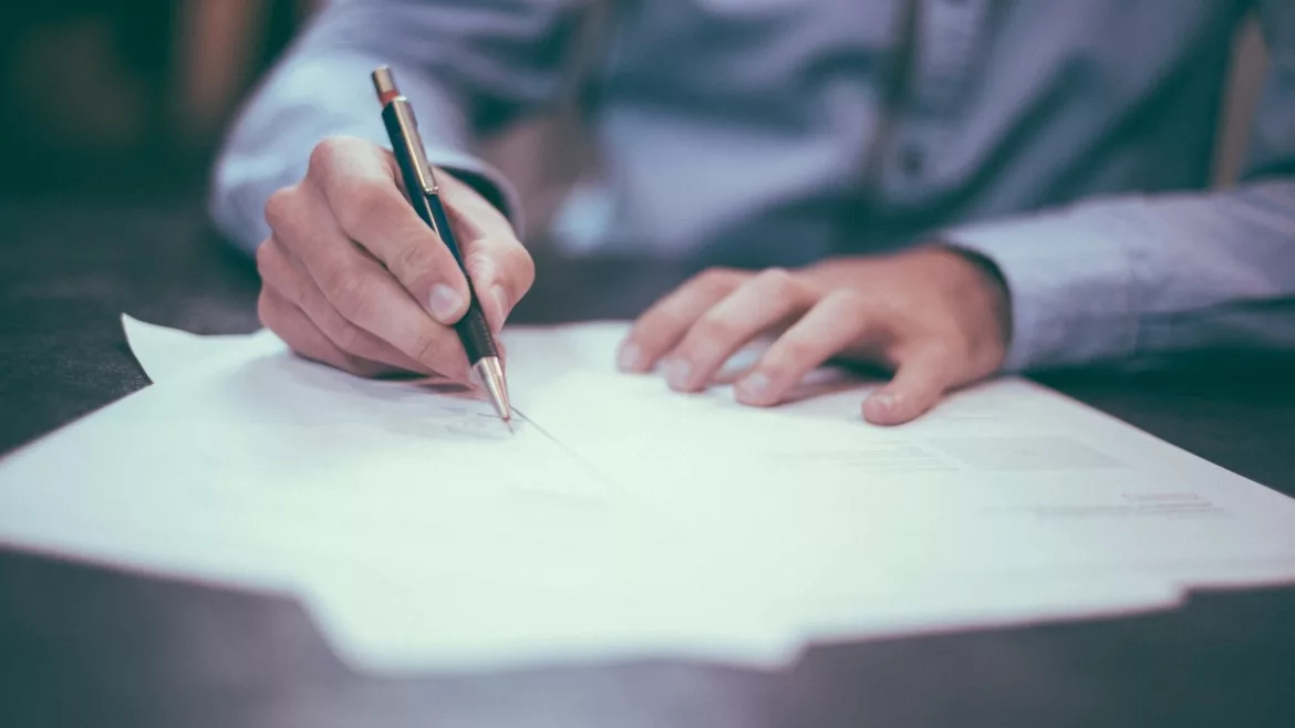 Image of a person writing on a stack of papers at a desk.