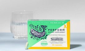 Greenfilled's capsule TetraSOD supplement packaging in front of a glass of water.