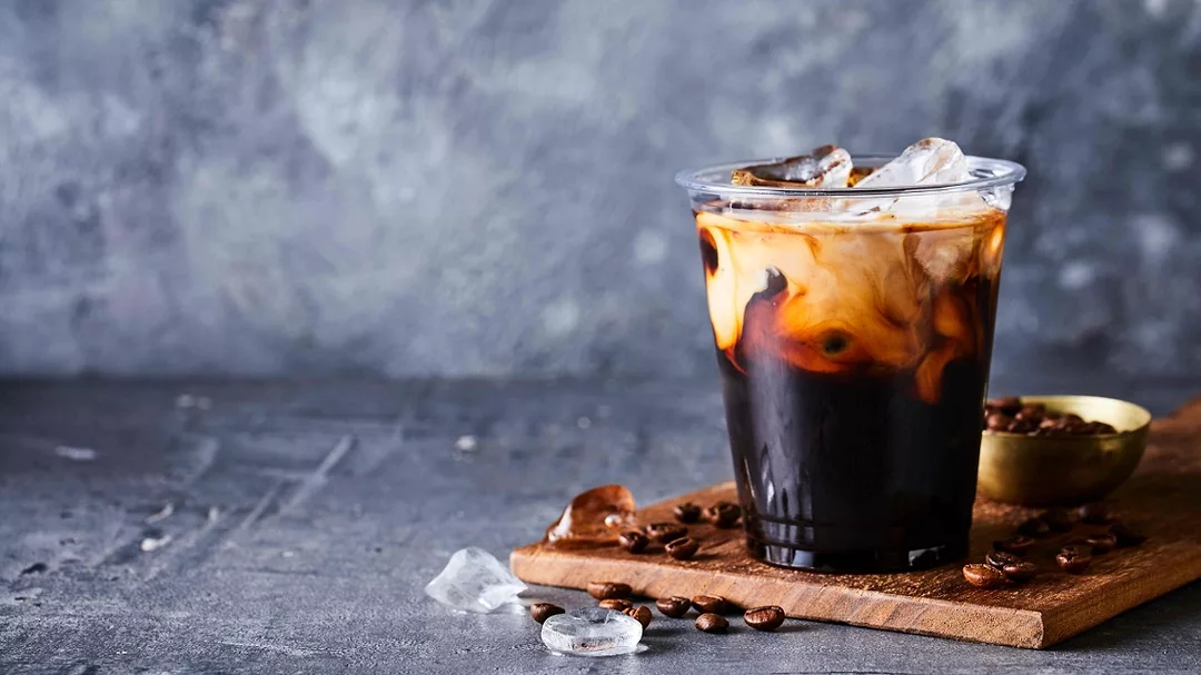 Kerry's Coffee Beverage sweetner in a clear glass of coffee in front of a blue background.