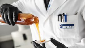 Image of a person in a Hi-Food lab coat pouring a liquid from a glass container.