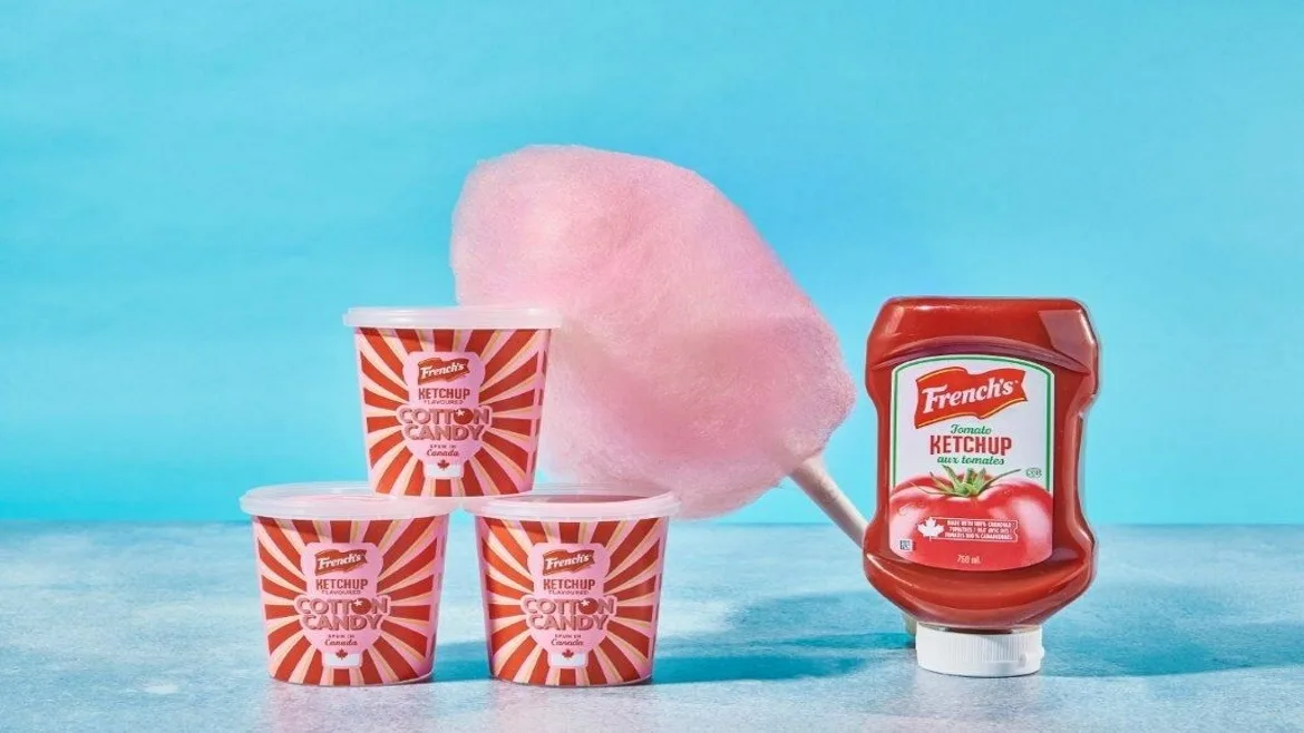 McCormick French's limited-edition Cotton Candy Ketchup with a bottle sitting next to 3 stacked tubs and a cone of cotton candy in the background.