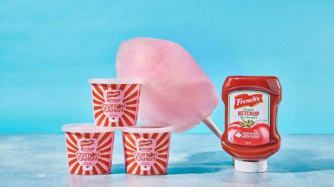 McCormick French's limited-edition Cotton Candy Ketchup with a bottle sitting next to 3 stacked tubs and a cone of cotton candy in the background.