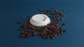 PulPac's dry-molded fiber coffee lid on top of a pile of coffee beans.