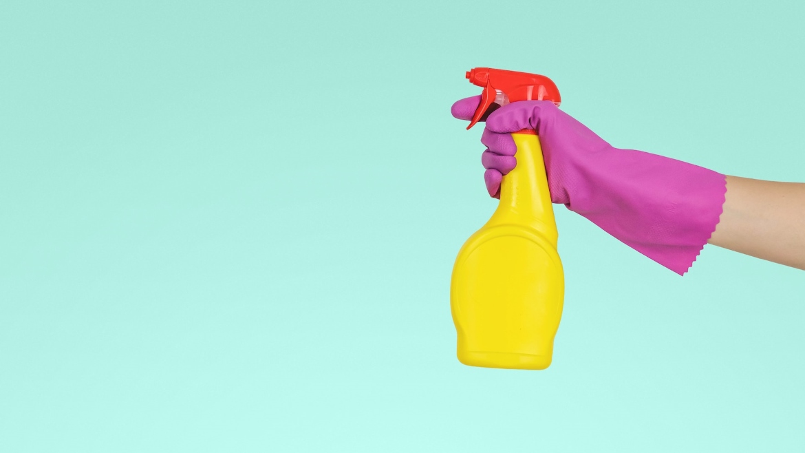A yellow and pink spray bottle held by a person wearing a glove