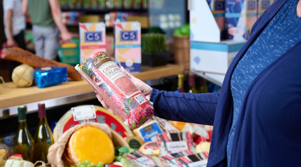 a woman in a grocery store holding salami with a QR code