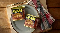 Two SPAM maple flavored cans next to a plate with a fork and knife Two SPAM maple flavored cans next to a plate with a fork and knife