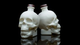 Two skull-shaped vodka bottles on a black surface and background