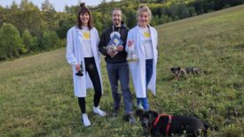 Image of three BioCraft leaders outside in a field next to two dogs.