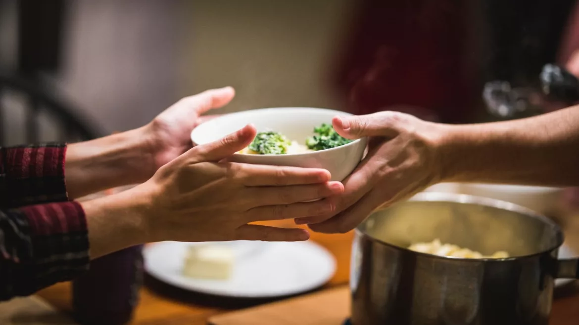 Two people passing food at a dinner table