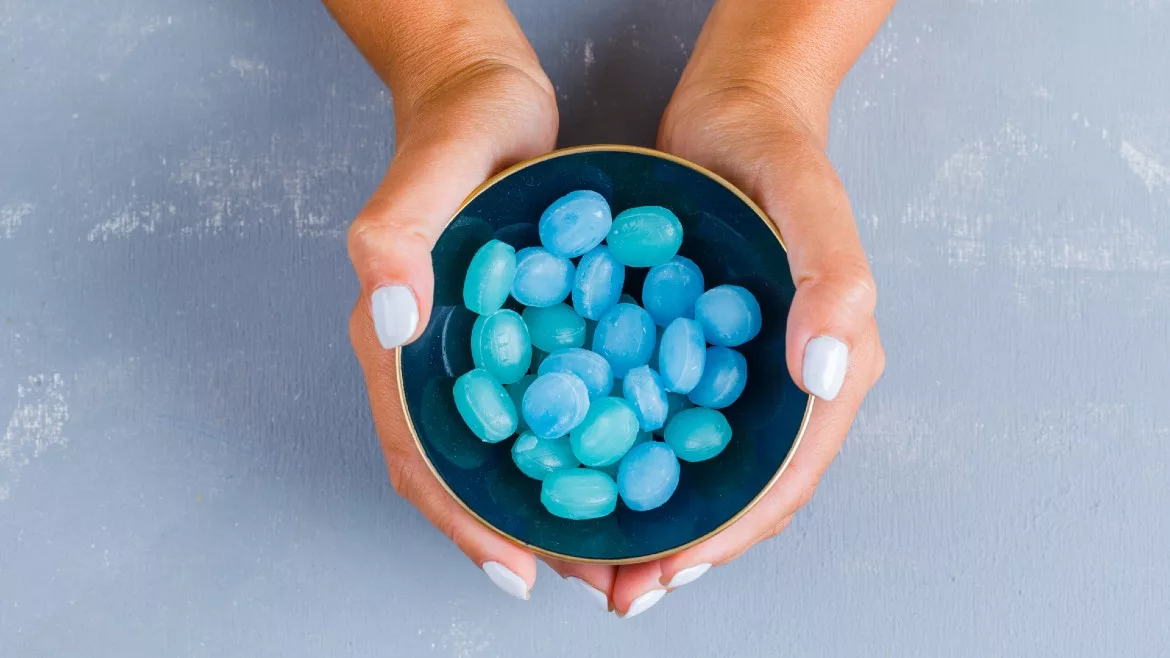 Hands holding blue candies in a bowl