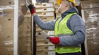 Warehouse worker scanning pallet labels while holding a clipboard.