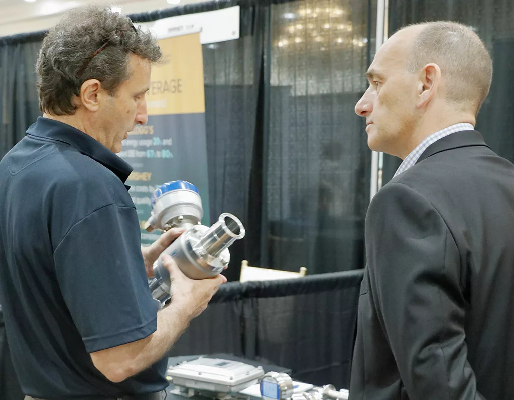 A Food Automation & Manufacturing Symposium and Expo exhibitor showing an attendee a piece of manufacturing equipment.