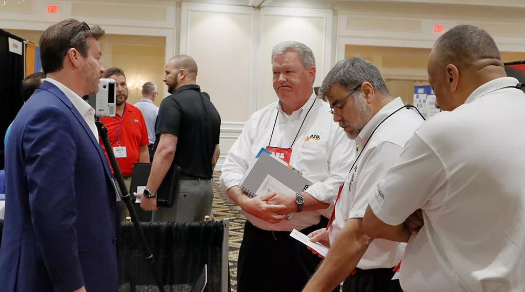 A Food Automation & Manufacturing Symposium and Expo exhibitor speaking with three attendees at their exhibiting booth.