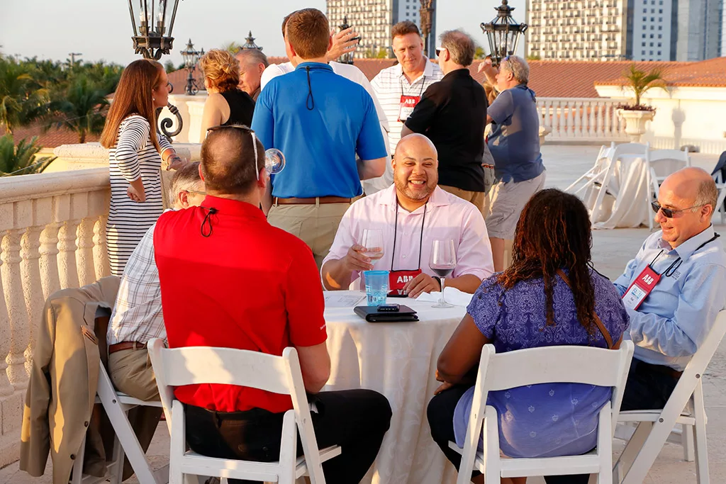 Food Automation & Manufacturing Symposium and Expo attendees sitting at a round table with drinks networking outside at the Doral Resort in Miami.