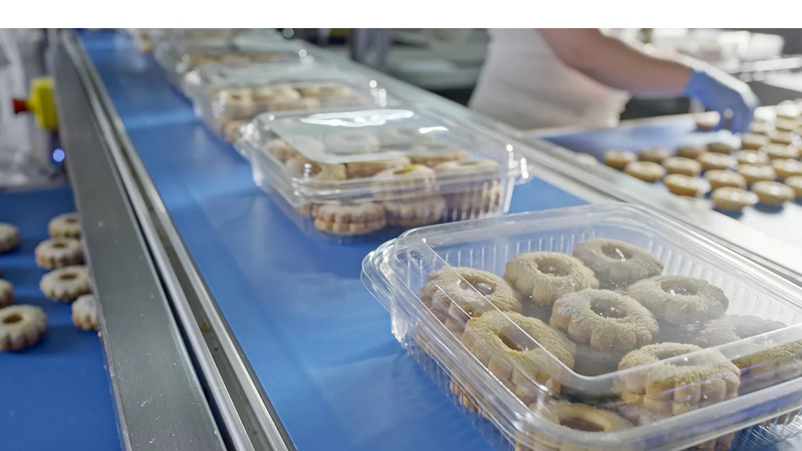 Plastic packaged cookies on a conveyor belt Close-up view of transparent plastic containers filled with cookies moving along a blue conveyor belt in a production line.