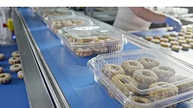 Close-up view of transparent plastic containers filled with cookies moving along a blue conveyor belt in a production line.