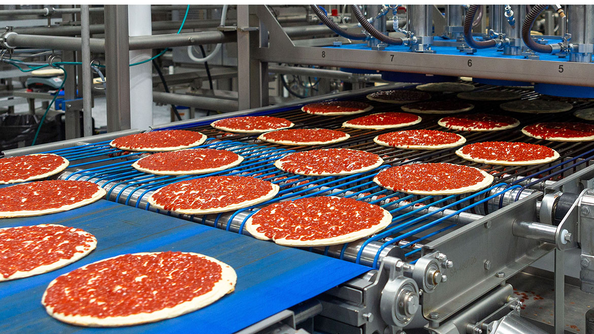 Pizzas with red sauce on a conveyor belt in a food processing factory, showing automated production.
