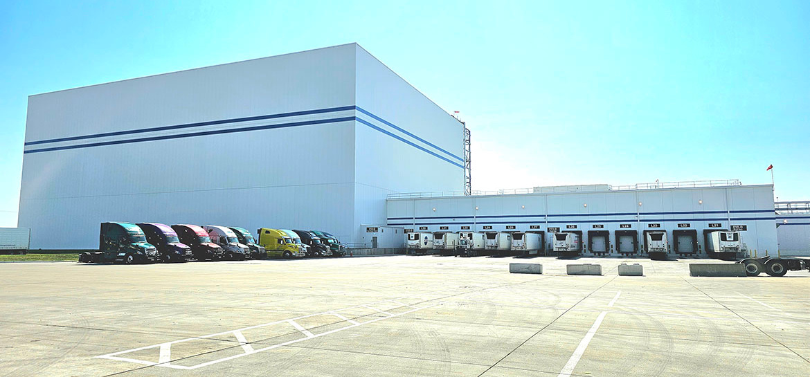 Exterior of CJ Schwan’s new, 140,000-sq.-ft. distribution center, showing loading docks, and a line of colorful semi-trucks parked in a parking lot.