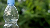 Close up of blue water bottle outside with a blurred background showing greenery.