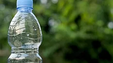 Close up of blue water bottle outside with a blurred background showing greenery.