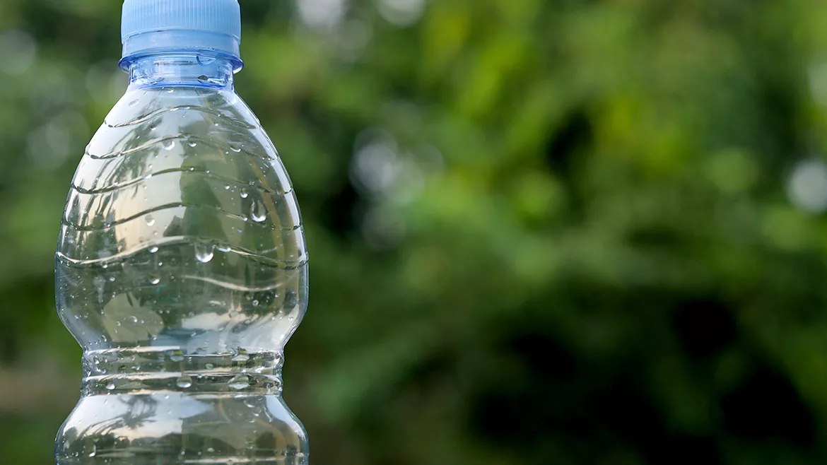 Close up of blue water bottle outside with a blurred background showing greenery.
