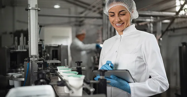 Technician inspects products in a dairy manufacturing assembly line. Another technician is shown in the blurred background.