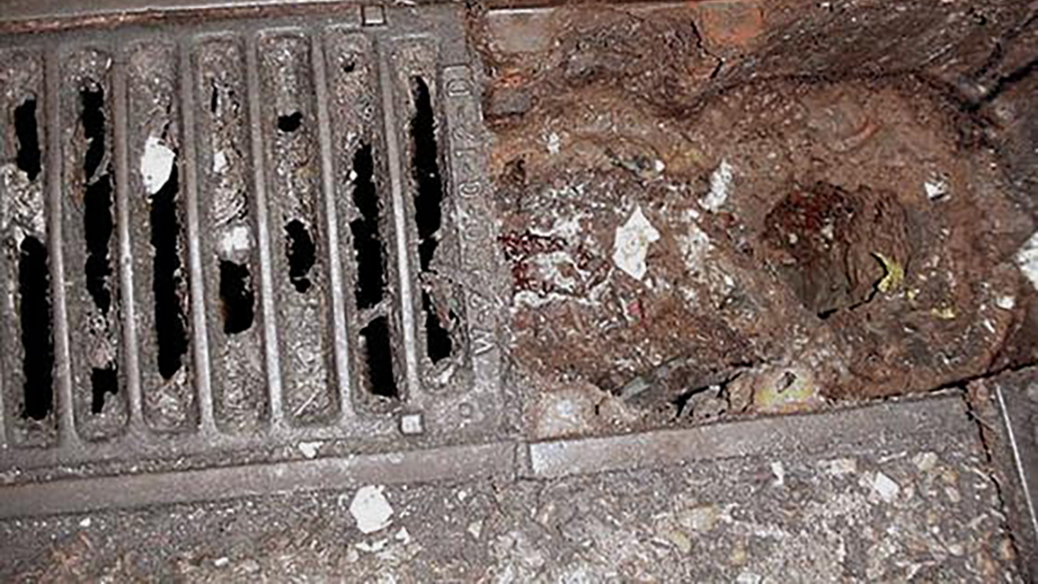Overhead image of a trench drain full of dirt and waste on the floor.