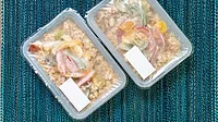 Two plastic containers with clear, plastic seals filled with rice and vegetables on a green tablecloth.