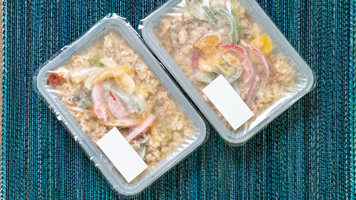 Two plastic containers with clear, plastic seals filled with rice and vegetables on a green tablecloth.
