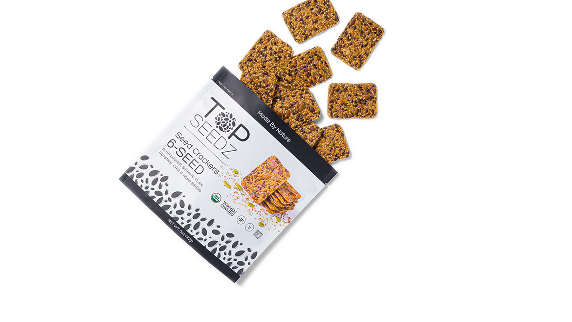 An angled Top Seedz packet of crackers, open at the top with crackers spilling out on a white background.