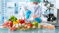 Food scientist in a lab with fresh food. A food scientist in protective clothing and eye gear is working in a lab and examining petri dishes, fresh vegetables, fruits, seeds, eggs and meet in from of her.