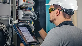 Worker in a white safety hat and glasses is using a digital tablet to examine equipment.