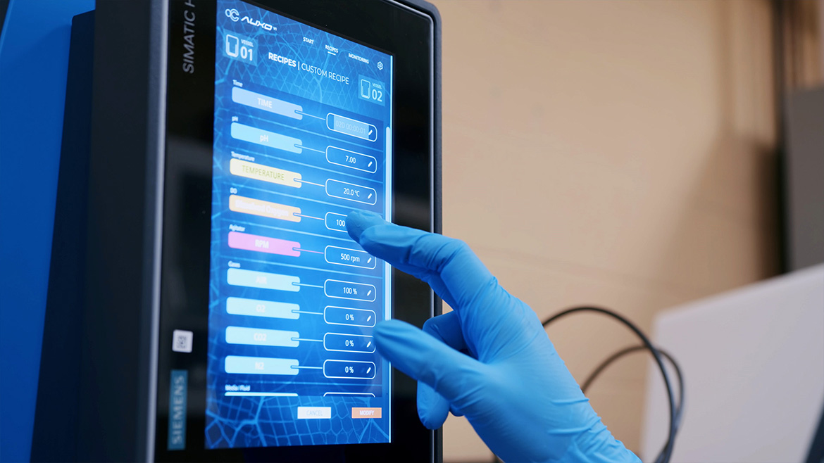 A hand with a blue nitrile glove on, using the Siemens recipe management.