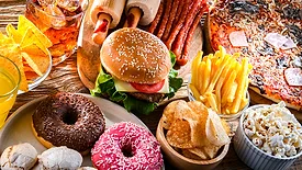 A table of food considered 'junk food' such as pizza, cheeseburger, fries, donuts, meat sticks, and chips.