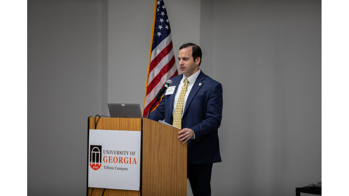 Image of Chris Chammoun delivering a speech behind a podium that has “The University of Georgia, Tifton Campus” on it.