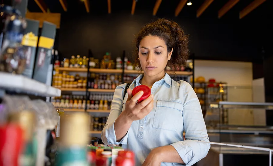 Image of a woman looking at the label of a grocery product in the produce isle of a grocery store