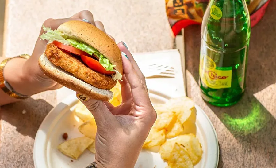 A woman holding a Rebellyous chicken patty burger at a picnic table