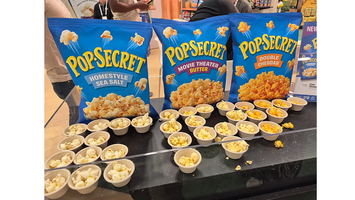 Samples of PopSecret popcorn in blue bags, at the 2025 Sweets & Snacks Expo.