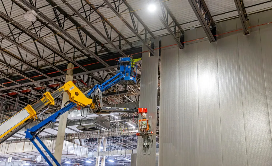 Construction crews use aerial lifts to install insulated wall panels inside an industrial facility.