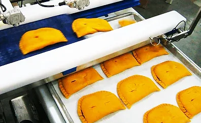 Close-up of a group of freshly baked stuffed empanadas being transferred onto a conveyor belt.
