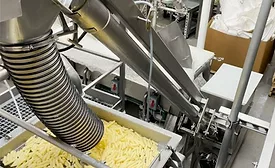 Stainless steel conveyor system transferring cut food pieces—likely pasta or fries—through an enclosed industrial processing line using a flexible hose and screw conveyor in a manufacturing facility.
