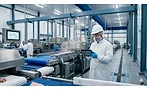 Worker in protective food-processing attire uses a tablet beside stainless-steel conveyor equipment in a modern food manufacturing facility.