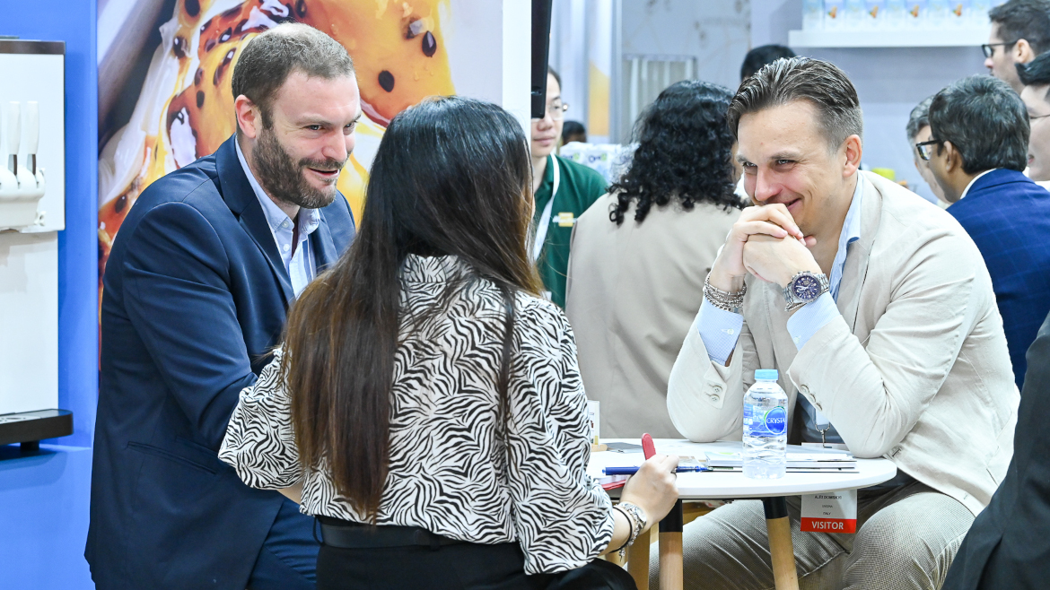 Two men and a woman are sitting at a table, both men are looking at the woman and smiling.