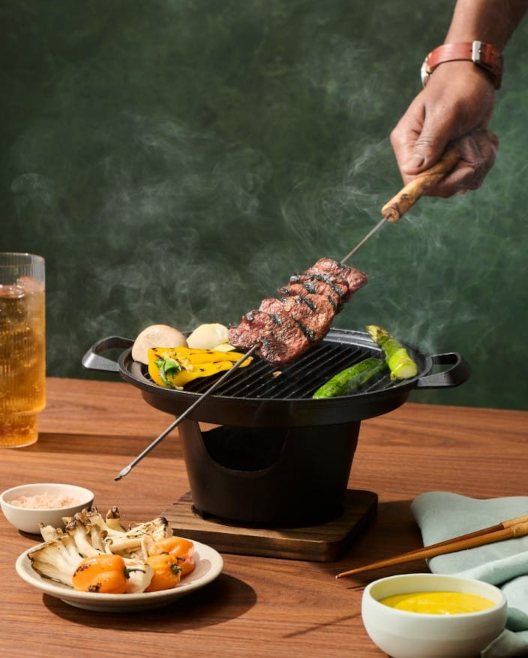 An Aleph Cuts on a skewer being barbecued on a tabletop barbecue.